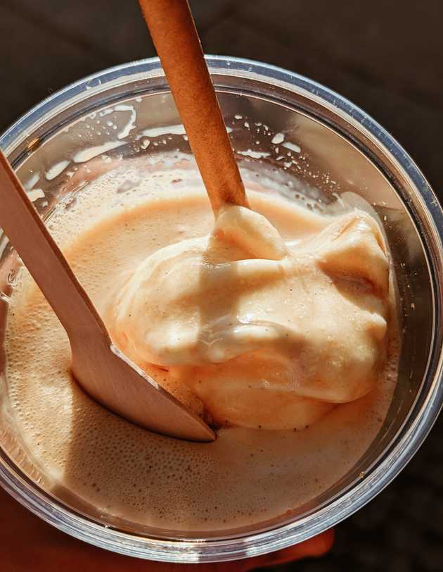 A plastic cup containing black coffee, a scoop of vanilla ice cream, a wooden spoon and a paper straw